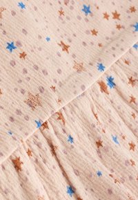 Un tissu rose clair avec une surface texturée, orné de petites étoiles bleues et brunes et d'un motif de points dispersés dans des teintes variées.