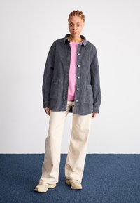 Sivá kordúrová bunda s gombíkmi, nášivkovými vreckami a golierom, vrstvená cez ružový sveter. Béžové široké nohavice a svetlé topánky.