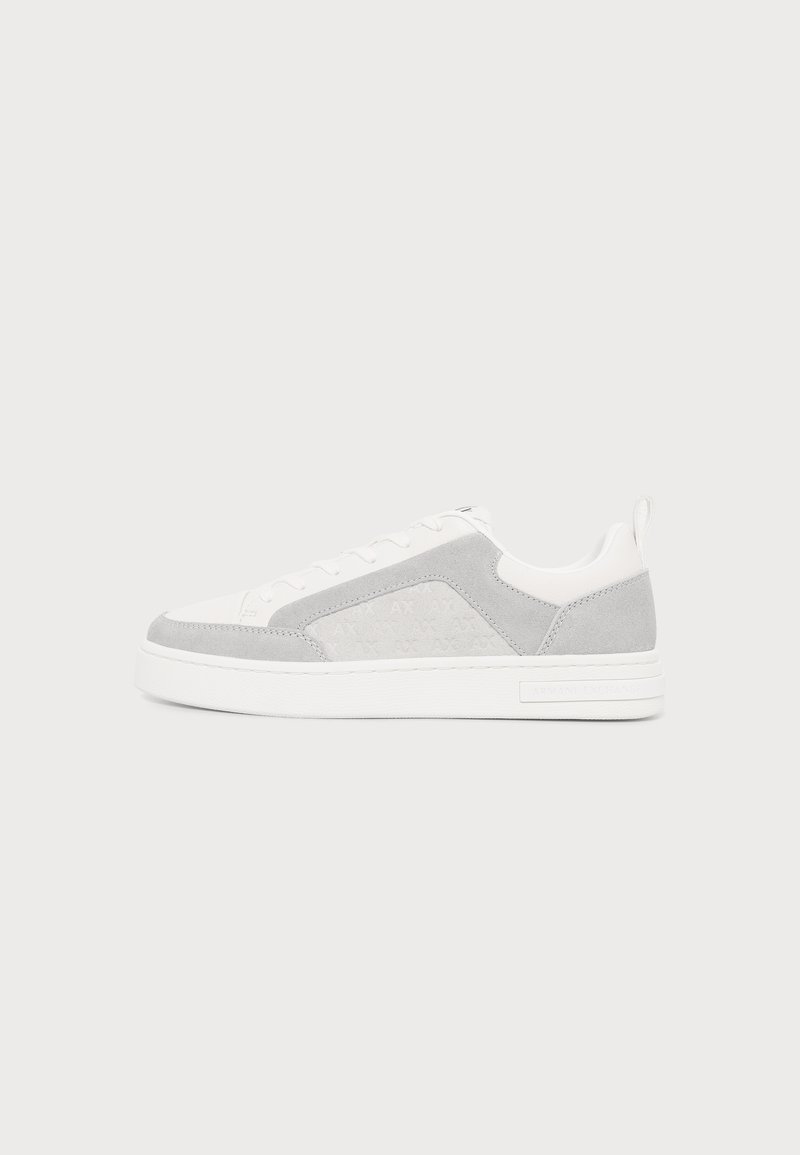 Baskets basses blanches avec des panneaux en daim gris clair, des lacets blancs et une semelle en caoutchouc blanche sur un fond clair uni.