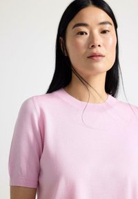 Maglione corto a maniche corte di colore rosa chiaro, con scollatura rotonda e texture liscia. Presenta una silhouette aderente e polsini a coste.