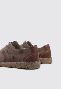 Zapatos de ante marrón con diseño perforado, detalles en cuero marrón y una suela de corcho texturizada. Presentan costuras en contraste y un estilo sin cordones.