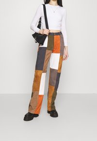 Patchwork-Hose aus Wildleder mit orangen, braunen, grauen und weißen Paneelen; kombiniert mit einem enganliegenden weißen Langarmtop und einer schwarzen Tasche.