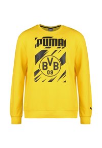 Żółta bluza z bawełny z czarnymi grafikami. Posiada okrągły dekolt, długie rękawy oraz ściągacze na rękawach i u dołu. Obecne logo i szczegóły drużyny.