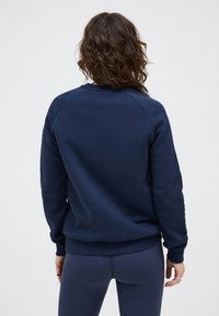Marineblauwe sweatshirt van zacht materiaal, met een ronde hals en ribbelboorden. De achterkant toont een naadloos ontwerp met raglan mouwen.