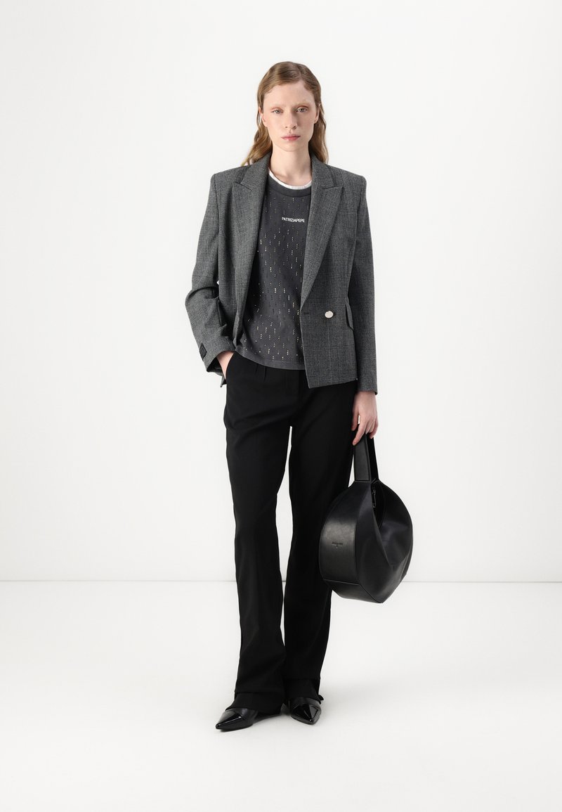 Szary marynarka w kratę z pojedynczym guzikiem, w połączeniu z ciemnym t-shirtem z grafiką, czarnymi dopasowanymi spodniami oraz okrągłą czarną torebką.