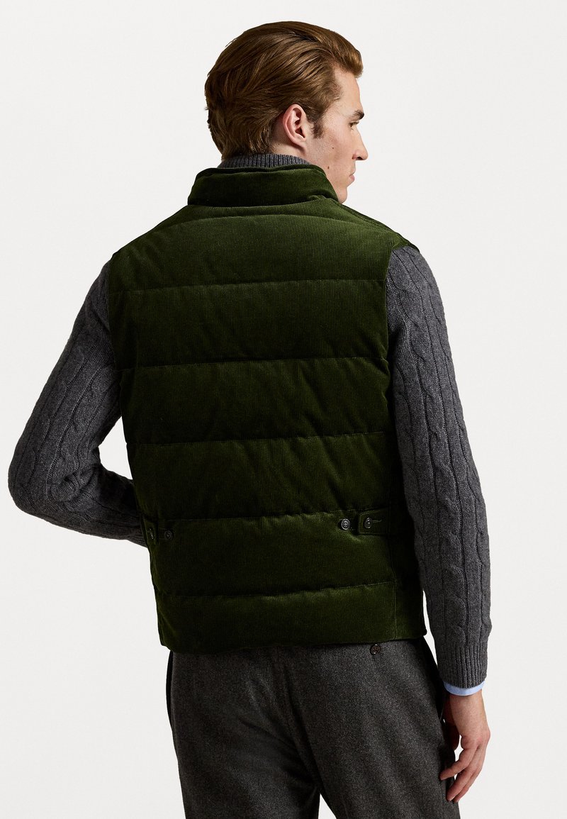 Grüne Corduroy-Puffweste mit horizontalen Nähten und Knopfdetails. Getragen über einem grauen Kabelstrickpullover, mit Kragen und glatter Textur.