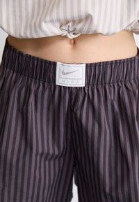Nike sportbroekjes in donkergrijs met verticale strepen. De tailleband van elastiek heeft een label met logo. Het materiaal lijkt lichtgewicht en glad.