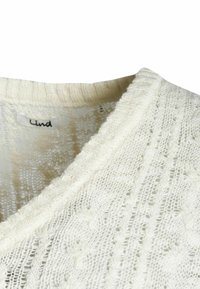 Cremfarbener gestrickter Pullover mit V-Ausschnitt, strukturierten Mustern und Rippakzenten entlang des Kragens und der Kanten. Markenetikett sichtbar.