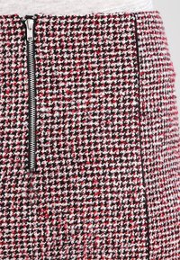Jupe en tweed tissée avec un motif à carreaux rouge, noir et blanc. Comprend une fermeture éclair sur le côté et une surface texturée avec des épaisseurs de fil variées.