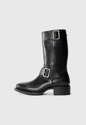Schwarze, knöchelhohe Lederstiefel mit runder Spitze, silbernen Schnallenakzenten und einem blockartigen Absatz. Sie haben eine glatte Textur und einfache Linien.