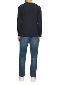 Marineblaues Langarmshirt, kombiniert mit hellblauen Jeans. Die Jeans haben Gesäßtaschen und weiße Sneaker werden getragen.