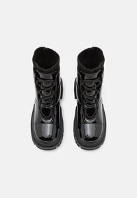 Bottines noires à lacets avec une finition patinée brillante, semelles en caoutchouc et une manchette tricotée à la cheville pour un soutien et un confort supplémentaires.