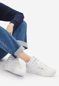 Kerged valged tossud siledast nahast, seotud ja olnud takjapaelaga, augud varvaste juures ja peened brändi aktsendid. Kandsid rullitud teksapükse.