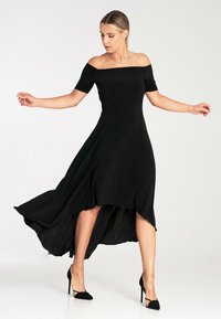 Czarna sukienka na ramiączkach, z krótkimi rękawami, ze swobodnym asymetrycznym dołem i gładką fakturą. W zestawieniu z czarnymi szpilkami.