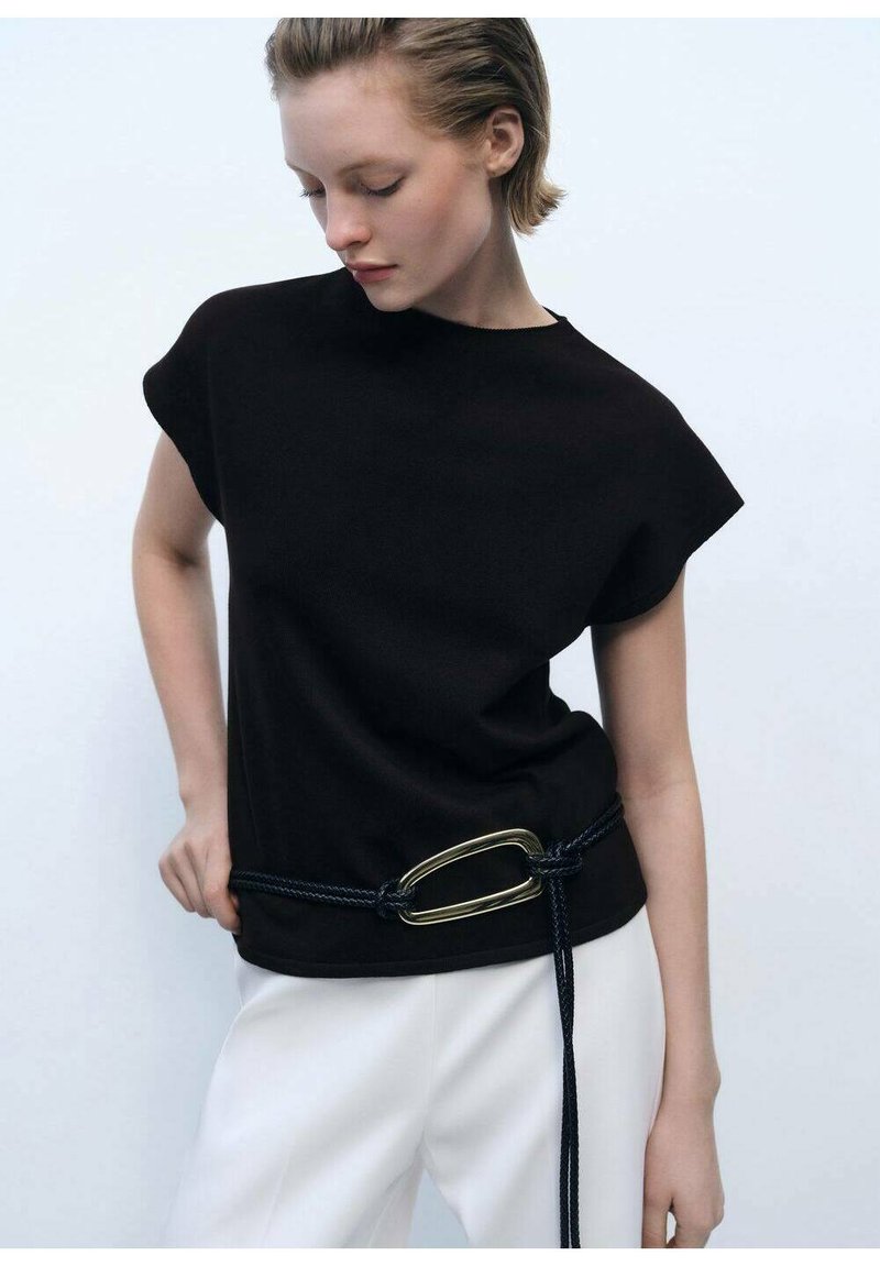Black short-sleeve top with a round neckline, paired with white pants. A navy rope belt with a large gold buckle accents the waist.