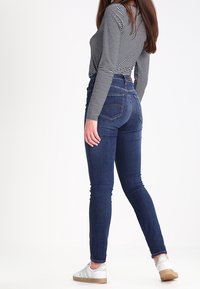 Höga mörkblå jeans med smal passform, sydda detaljer på bakfickorna, tillsammans med en svart och vit randig långärmad skjorta.