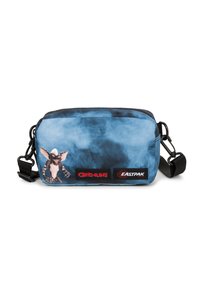 Blauwe tie-dye schoudertas met Gremlins-personageprint, zwarte verstelbare schouderband, en rode Gremlins en Eastpak logo-patches op de voorkant.