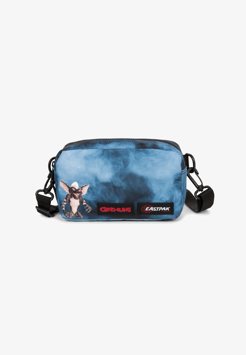 Blauwe tie-dye schoudertas met Gremlins-personageprint, zwarte verstelbare schouderband, en rode Gremlins en Eastpak logo-patches op de voorkant.
