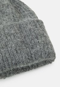 Siva pletena kapa iz mehkega volnenega materiala, ki ima teksturiran vzorec in zloženi rob na dnu za dodatno toploto.