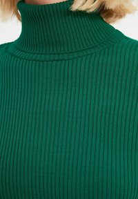 Grüner gerippter Rollkragenpullover mit schmaler Passform. Die Stofftextur ist weich und weist auffällige vertikale Streifen sowie einen hohen Kragen auf.
