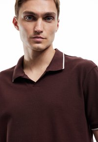Mörkröd polotröja med en texturerad tyg, som har en V-formad öppning och kontrasterande vit kant på kragen.