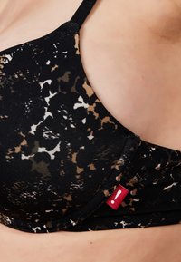 Zwarte en bruine beha met een patroon en een soepele textuur, voorzien van een rode accentlabel. Verstelbare banden en een afgeronde vorm.