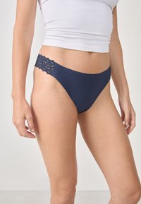 Slip bikini blu navy con un materiale liscio e una vita con fondo in pizzo a motivi floreali, che mette in risalto una vestibilità elasticizzata.