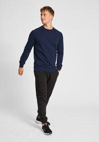 Navyblauwe sweatshirt met lange mouwen, geribbelde manchetten en onderkant, gecombineerd met zwarte joggingbroeken en zwarte sneakers. Eenvoudig, casual ontwerp.