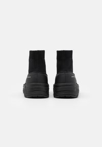 Svarta anklarstövlar med stickad ovandel och gummisula, med en slät textur och subtil branding på hälen.