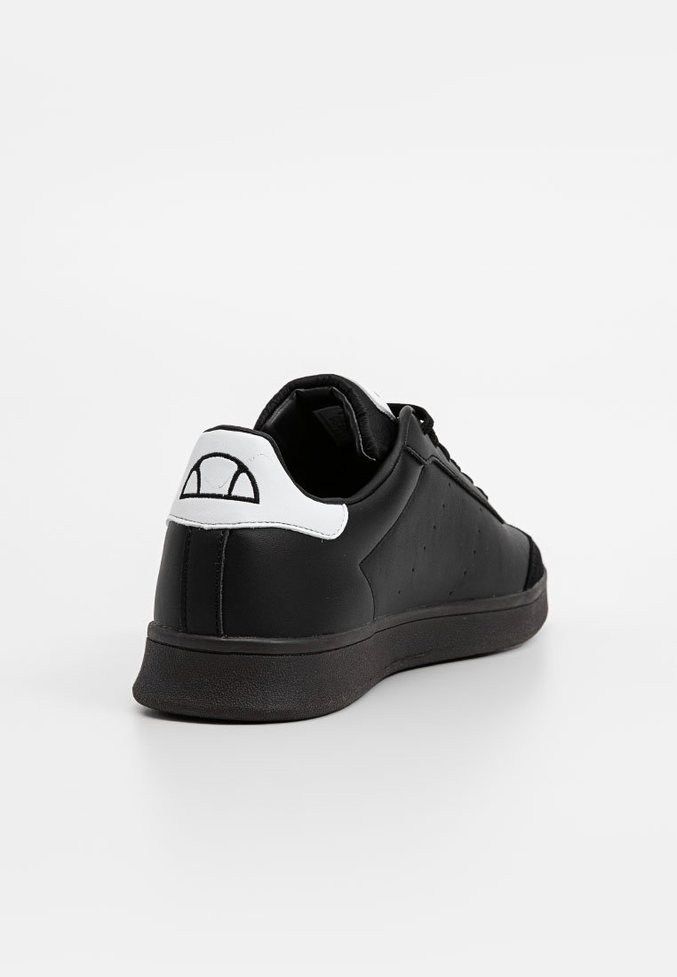 Zapatilla de cuero negro con textura suave, acento blanco en el talón y logotipo, puntera redonda y suela de goma plana. Con perforaciones en los laterales para transpirabilidad.