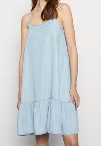 Světle modré bezramenné šaty vyrobené z měkké tkaniny, s rozšířeným tiered lemem a jemným šitím podél výstřihu a armhole.