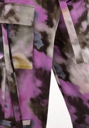 Gros plan sur un tissu tie-dye violet et noir avec une poche et des longues lanières de tissu pendant librement.