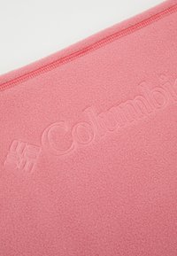 Tissu en polaire rose avec une surface texturée, arborant un logo « Columbia » en relief et de subtils détails de couture le long du bord.