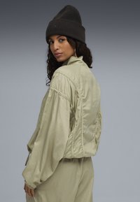 Veste bomber vert clair avec une coupe décontractée, en tissu texturé, épaules tombantes et poignets froncés. Associée à un bonnet en maille foncé.