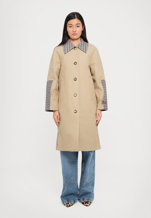Beige jas met een grote geruite kraag en geruite accenten op de mouwen. Voorzien van grote knopen en zijzakken, met een rechte snit.