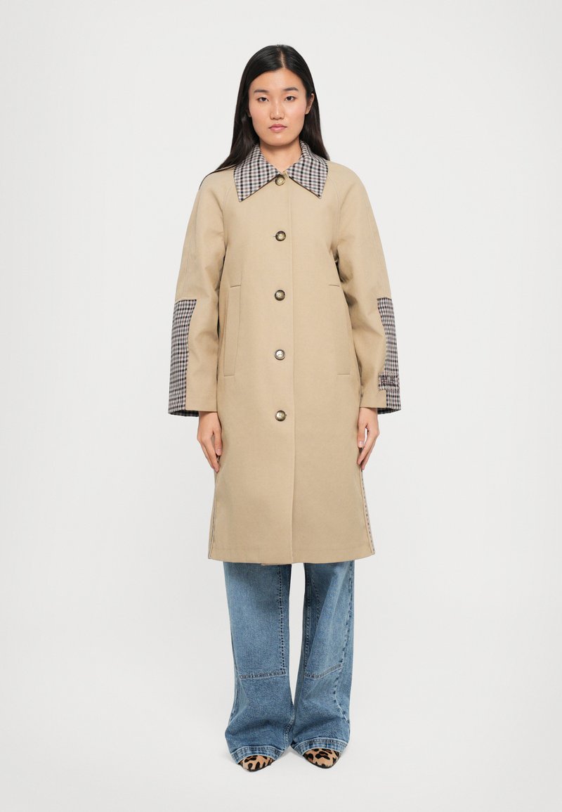 Beige coat with a large checked collar and checkered pattern accents on sleeves. Features large buttons and side pockets, with a straight cut.