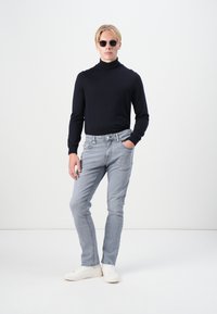 Schwarzer Rollkragenpullover, hellgraue taillierte Jeans, weiße Sneakers und runde Sonnenbrille. Glatte Textur und modernes Silhouette.