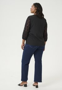 Black top with lace three-quarter sleeves, paired with blue straight-leg jeans. The outfit features a smooth texture and tailored fit.