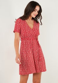 Rotes Blumenkleid mit kurzen Ärmeln, V-Ausschnitt und figurbetontem Taillenbereich. Leichter Stoff mit einem verstreuten Muster aus weißen und rosa Blumen.