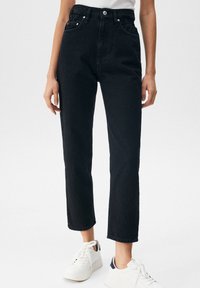 Jean en denim noir taille haute avec cinq poches, coupe droite, et légère usure. Associé à des baskets blanches.