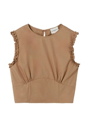 Femme portant un haut sans manches beige et un pantalon large avec des côtés décoratifs, ceinture rouge en foulard, tenant un sac à main beige tissé, debout.