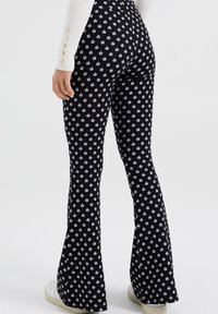 Černé rozšiřující se kalhoty s malým bílým květinovým vzorem. Vyrobeno z elastické tkaniny, s přiléhavým pasem a hladkou texturou.