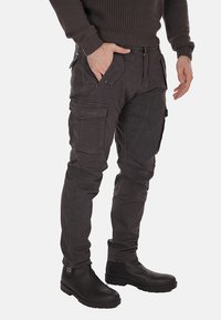 Pantaloni cargo grigi realizzati in tessuto resistente, con diverse tasche, design affusolato e superficie testurizzata. Indossati con stivali neri alla caviglia.