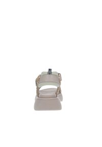 Sandalia beige con una suela acolchada, correas de textil y acentos decorativos de cuentas. Cuenta con una correa ajustable en el talón para mayor comodidad.
