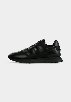 Μαύρο δερμάτινο sneaker χαμηλού ύψους με υφασμάτινες επιφάνειες, δέσιμο με κορδόνια μπροστά και ανυψωμένη σόλα, εμφανιζόμενο από το πλάι σε απλό φόντο.