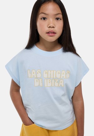 T-shirt en coton bleu clair avec texte jaune « LAS CHICAS DE IBIZA », manches courtes, col arrondi et coupe décontractée.