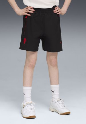 Svarta shorts med röda detaljer, utrustade med elastisk midja och sidofickor. Bärs med vita sneakers och ankelsockor.