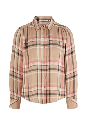 Persona con camisa de cuadros beige y suéter crema sobre los hombros, pantalones blancos de pierna ancha y mocasines marrones con suelas negras.