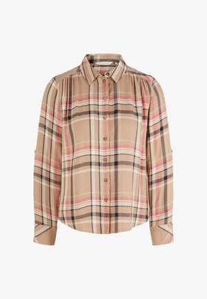 Personne portant une chemise à carreaux beige avec un pull crème drapé sur les épaules, un pantalon blanc à jambes larges et des mocassins marron avec semelles noires.