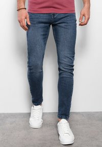 Jeans ajustados azules de denim, con un clásico diseño de cinco bolsillos. Combinados con zapatillas blancas para un look casual.